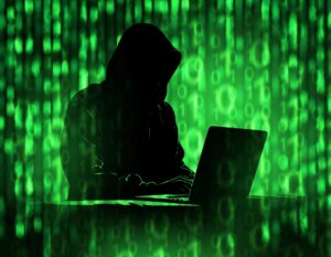 shadowy image of a hacker with green alphanumeric symbols around him representing code. 